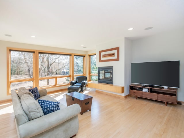 living area featuring recessed lighting, light wood-style flooring, baseboards, and a glass covered fireplace