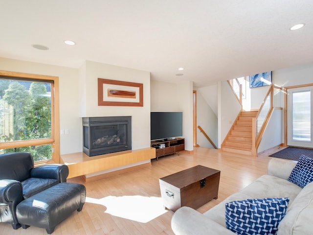 living area with stairs, a glass covered fireplace, wood finished floors, and recessed lighting