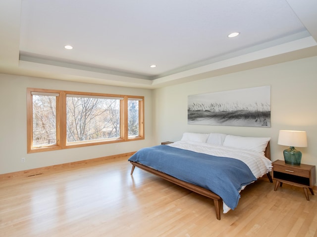 bedroom featuring recessed lighting, a raised ceiling, and light wood-style floors