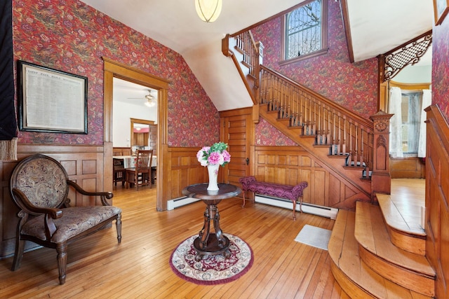 staircase with a wainscoted wall, wood-type flooring, baseboard heating, a baseboard heating unit, and wallpapered walls