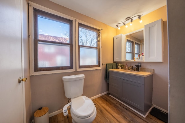 half bath with vanity, wood finished floors, toilet, and baseboards