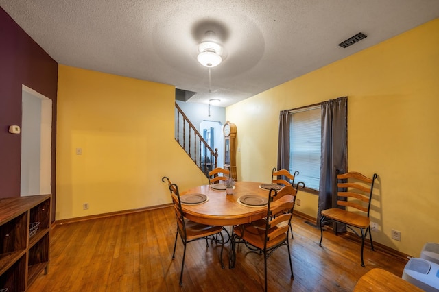 dining space featuring baseboards, visible vents, hardwood / wood-style flooring, stairway, and a textured ceiling