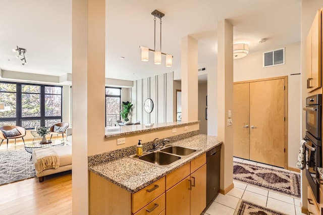 kitchen featuring visible vents, a sink, light stone counters, dishwasher, and hanging light fixtures