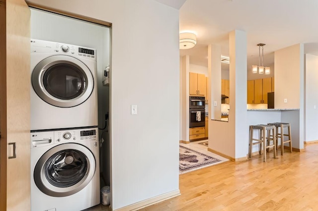 laundry area with laundry area, stacked washer / dryer, baseboards, and light wood-type flooring