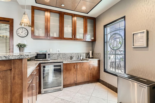 kitchen featuring a sink, stainless steel microwave, light stone counters, wine cooler, and brown cabinetry