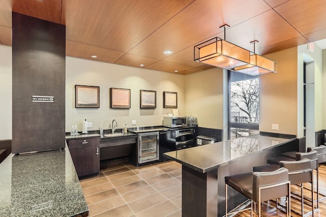 kitchen featuring stainless steel microwave, beverage cooler, a kitchen bar, a peninsula, and a sink