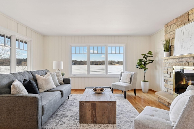 living area with a wealth of natural light, a stone fireplace, and wood finished floors