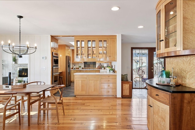 kitchen with stainless steel appliances, light wood-style flooring, light brown cabinets, a stone fireplace, and a chandelier