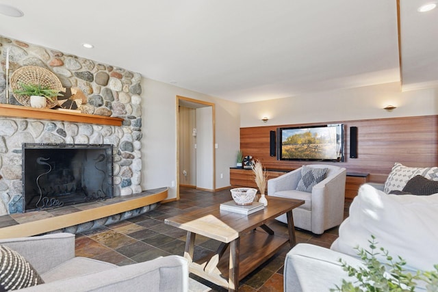 living area featuring baseboards, stone tile flooring, and a stone fireplace