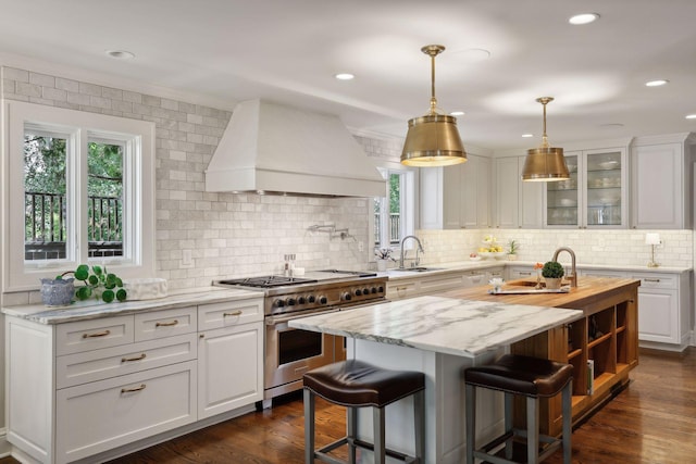 kitchen with range with two ovens, custom range hood, a sink, and white cabinetry