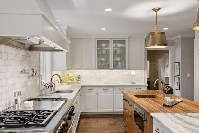 kitchen with glass insert cabinets, custom exhaust hood, stainless steel stove, white cabinetry, and a sink