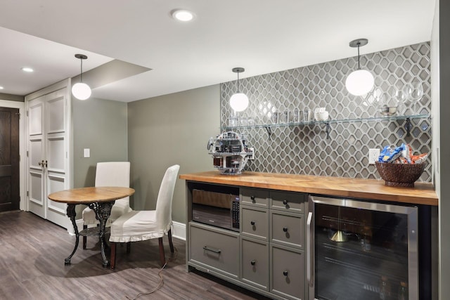 bar featuring tasteful backsplash, beverage cooler, dark wood-type flooring, a bar, and pendant lighting