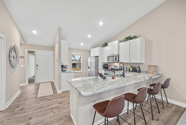 kitchen featuring appliances with stainless steel finishes, a kitchen breakfast bar, a peninsula, white cabinetry, and a sink