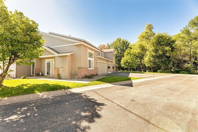 view of property exterior featuring brick siding, an attached garage, central air condition unit, a yard, and driveway