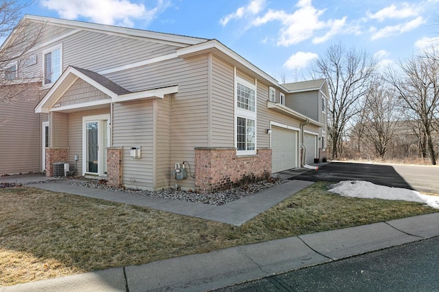 view of home's exterior with a yard, a garage, aphalt driveway, central air condition unit, and brick siding