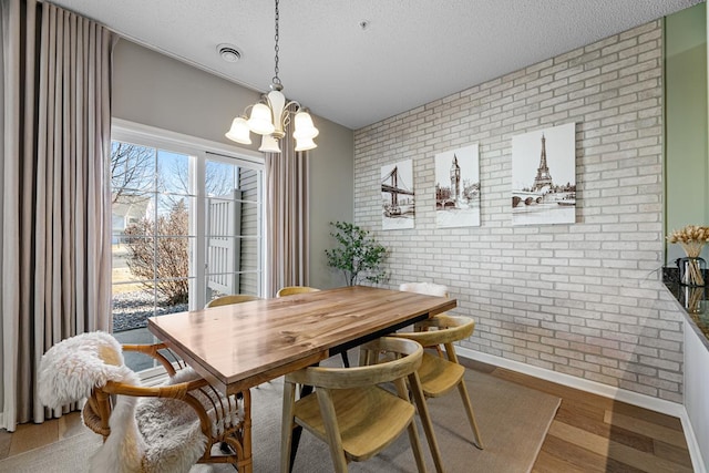 dining space with wood finished floors, visible vents, brick wall, and a textured ceiling