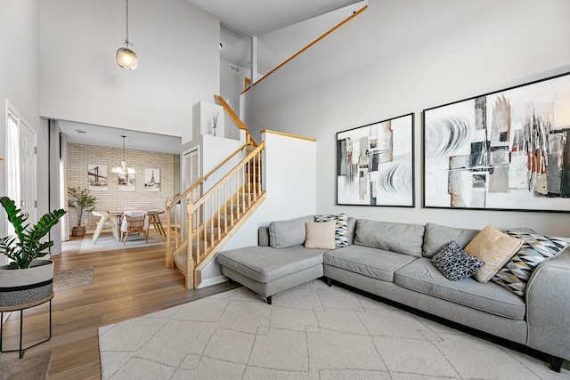 living room featuring stairway, wood finished floors, brick wall, an inviting chandelier, and a high ceiling