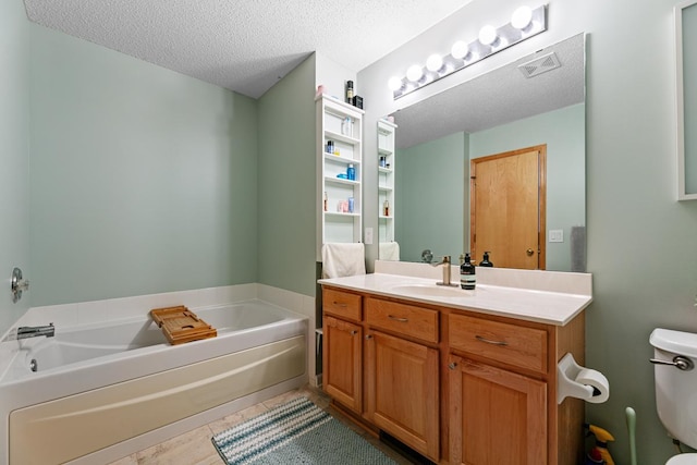 bathroom featuring visible vents, toilet, vanity, a garden tub, and a textured ceiling