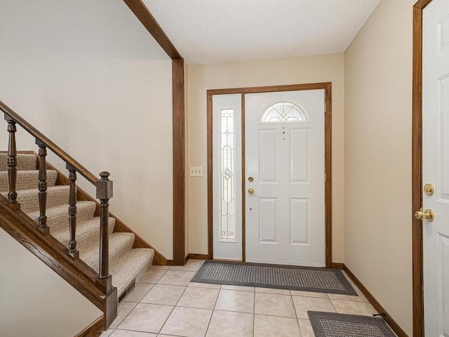 entryway with light tile patterned flooring, baseboards, and stairs