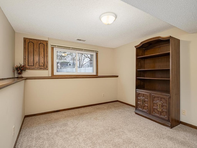 spare room with light colored carpet, visible vents, baseboards, and a textured ceiling