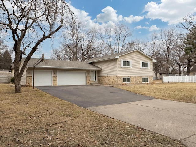 split level home with aphalt driveway, a garage, brick siding, fence, and a front yard