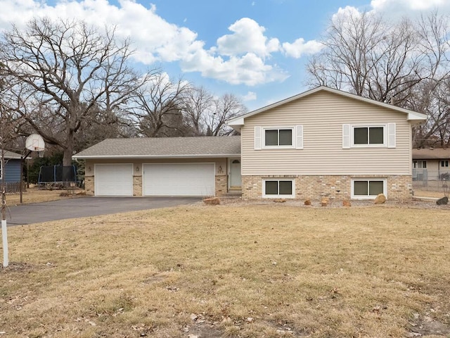 split level home featuring aphalt driveway, a front lawn, an attached garage, and brick siding