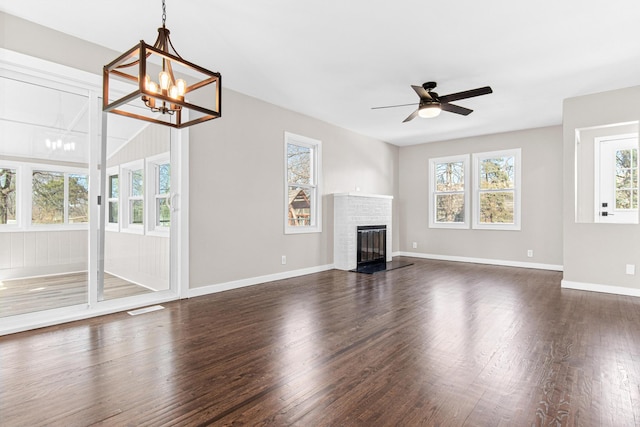 unfurnished living room featuring visible vents, ceiling fan with notable chandelier, dark wood finished floors, a fireplace, and baseboards