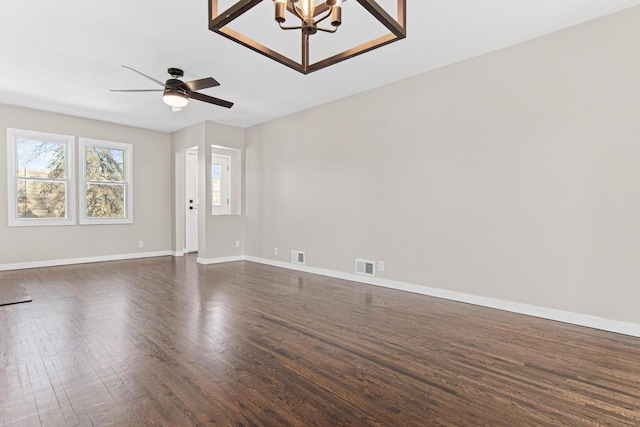 unfurnished room featuring ceiling fan with notable chandelier, baseboards, visible vents, and dark wood-style flooring