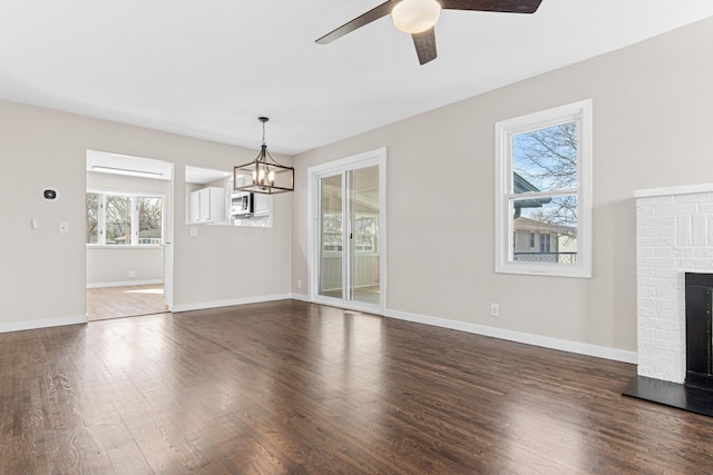 unfurnished living room featuring baseboards, dark wood-type flooring, a fireplace, and ceiling fan with notable chandelier