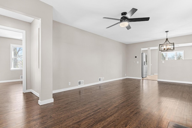 unfurnished living room with visible vents, baseboards, dark wood-style flooring, and ceiling fan with notable chandelier