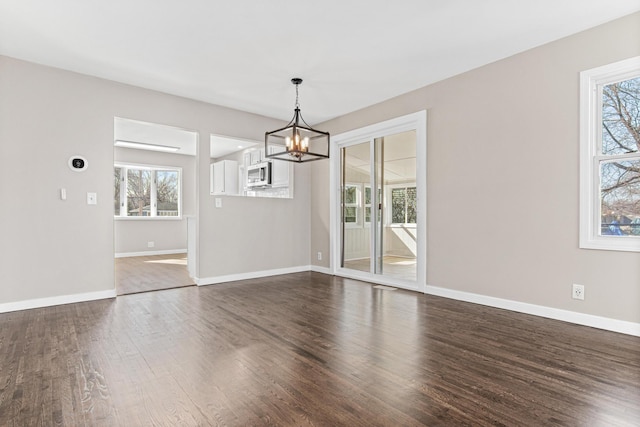 unfurnished dining area with baseboards, a notable chandelier, and dark wood-style floors