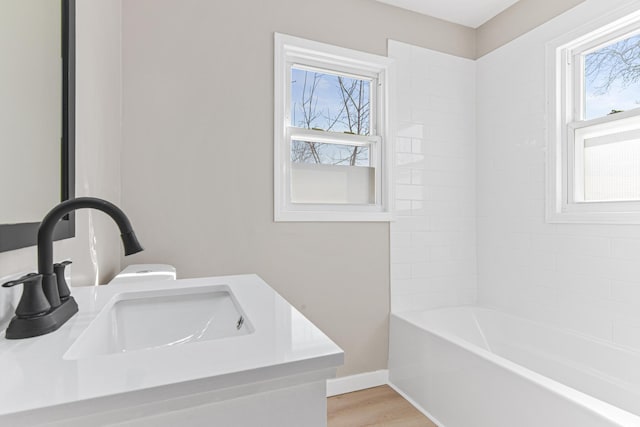 full bathroom featuring plenty of natural light, wood finished floors, baseboards, and a sink