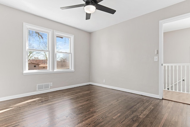 spare room with dark wood finished floors, visible vents, a ceiling fan, and baseboards