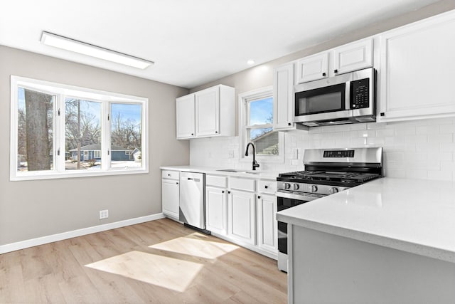 kitchen featuring tasteful backsplash, baseboards, light wood-style flooring, appliances with stainless steel finishes, and a sink