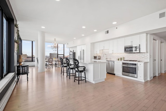 kitchen featuring a chandelier, a breakfast bar area, stainless steel appliances, light wood-type flooring, and backsplash