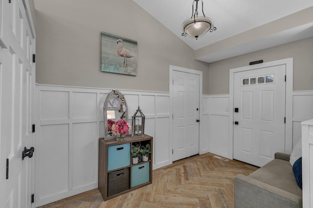 foyer with lofted ceiling, a wainscoted wall, and a decorative wall