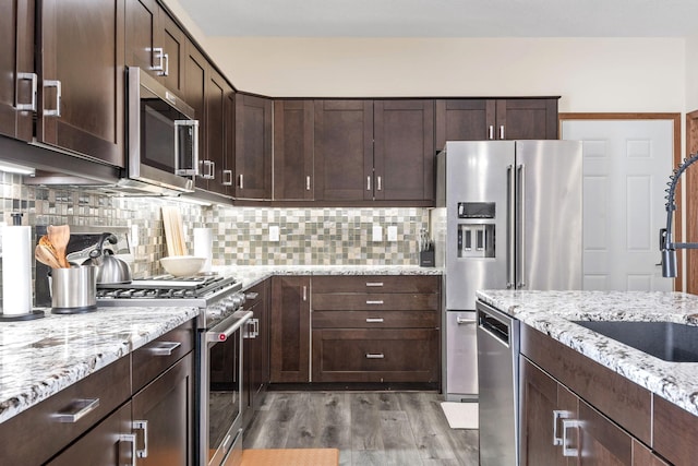 kitchen featuring backsplash, premium appliances, dark brown cabinets, and light wood-type flooring