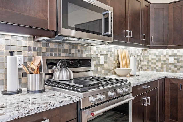 kitchen featuring dark brown cabinets, light stone countertops, tasteful backsplash, and appliances with stainless steel finishes