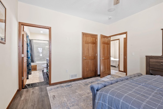 bedroom with visible vents, ensuite bath, baseboards, and wood finished floors