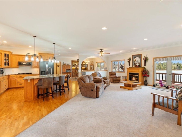 living area with crown molding, light carpet, recessed lighting, a warm lit fireplace, and arched walkways