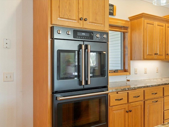 kitchen featuring double wall oven, light stone counters, and brown cabinetry