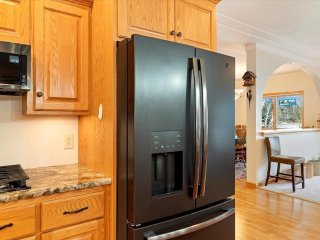 kitchen featuring light stone counters, arched walkways, stainless steel microwave, light wood-type flooring, and black refrigerator with ice dispenser