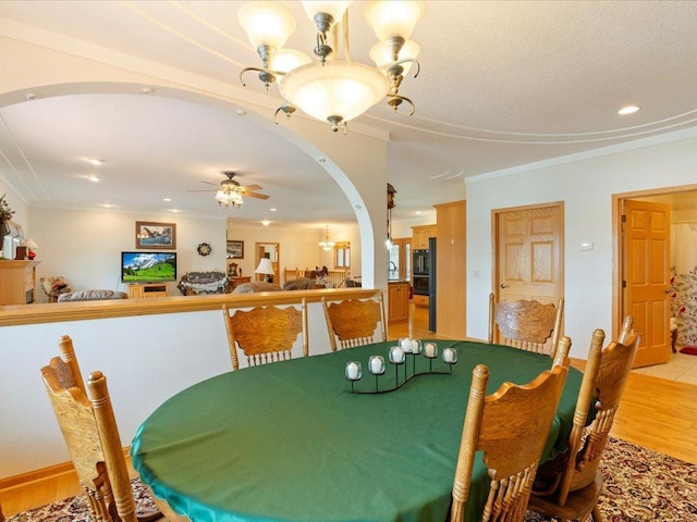 dining space with crown molding, ceiling fan with notable chandelier, arched walkways, and light wood finished floors