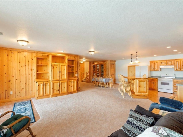 living room featuring wooden walls, light colored carpet, visible vents, and a textured ceiling