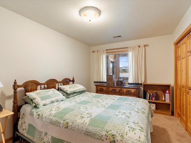 bedroom with a closet, visible vents, a textured ceiling, and light carpet