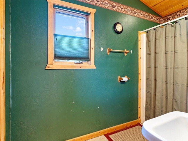 full bathroom featuring curtained shower, baseboards, lofted ceiling, and a textured wall