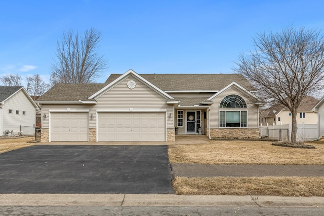 view of front of home with stone siding, an attached garage, fence, and driveway