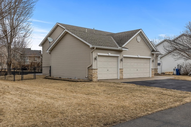 view of side of home with a garage, a shingled roof, a lawn, stone siding, and fence