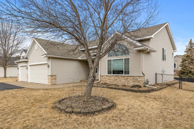 view of front facade featuring aphalt driveway, an attached garage, a shingled roof, fence, and stone siding