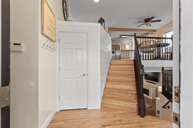 stairs with ceiling fan, beam ceiling, baseboards, and wood finished floors